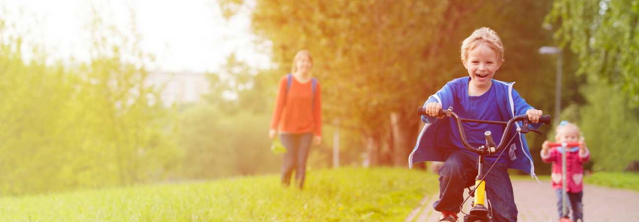 Young boy riding bicycle as mother and younger sister look on