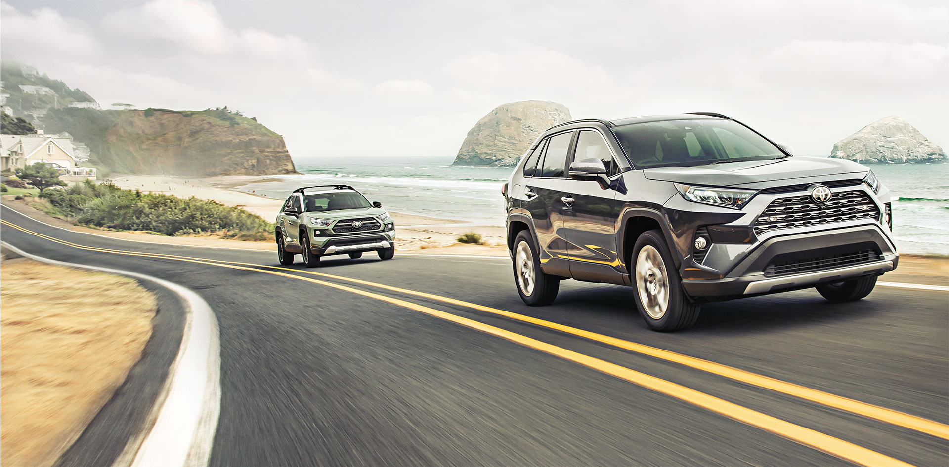 Two Toyota SUVs driving along a coastal road with ocean views